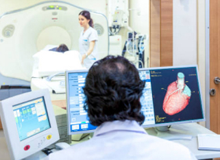 A healthcare professional monitors a patient's CT scan while another staff member prepares the patient for the procedure